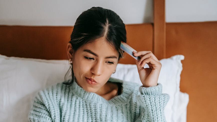 woman with credit card pondering while buying online with laptop